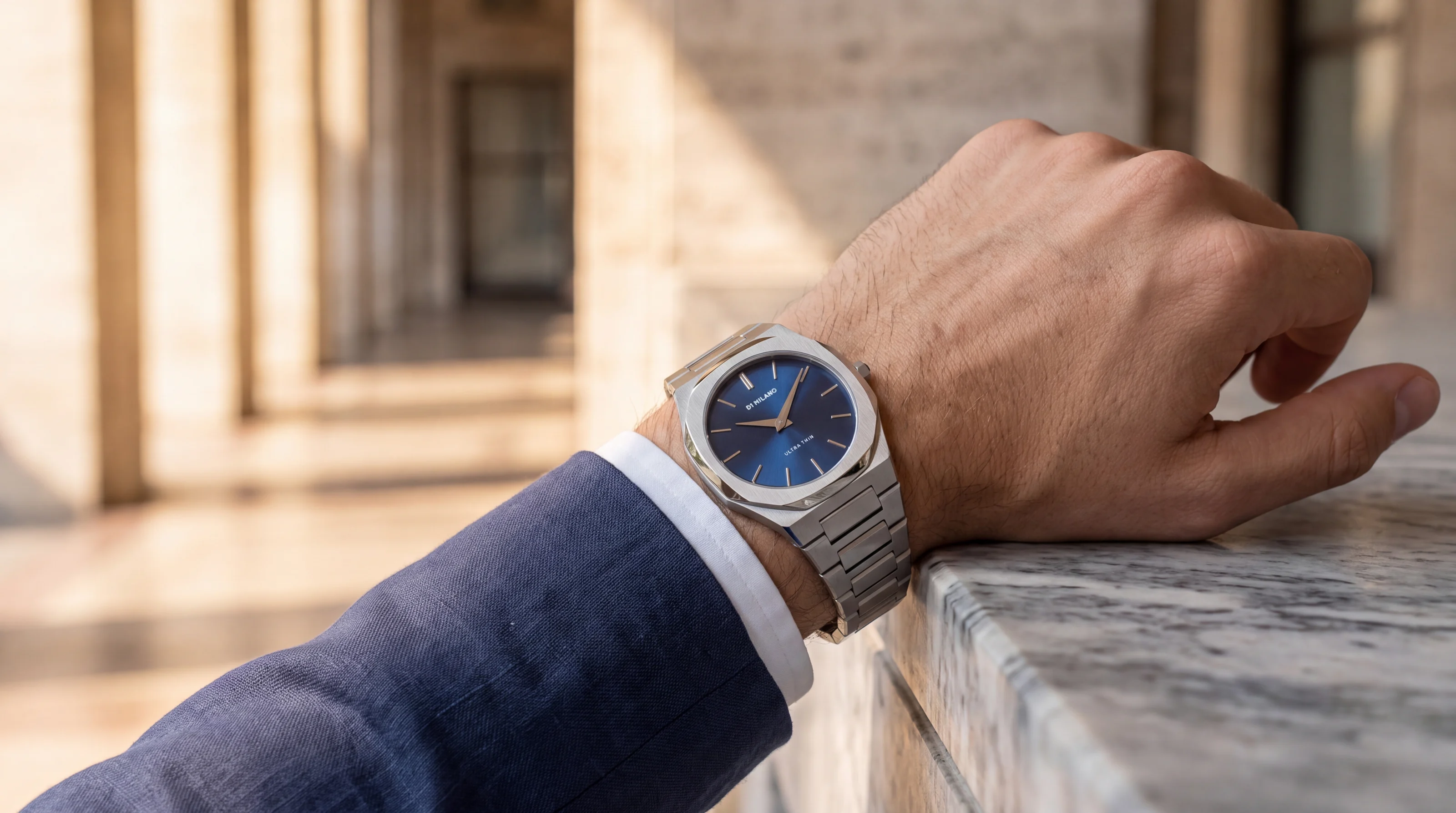 D1 Milano Ultra Thin watch with a blue dial worn on the wrist under a Milan colonnade