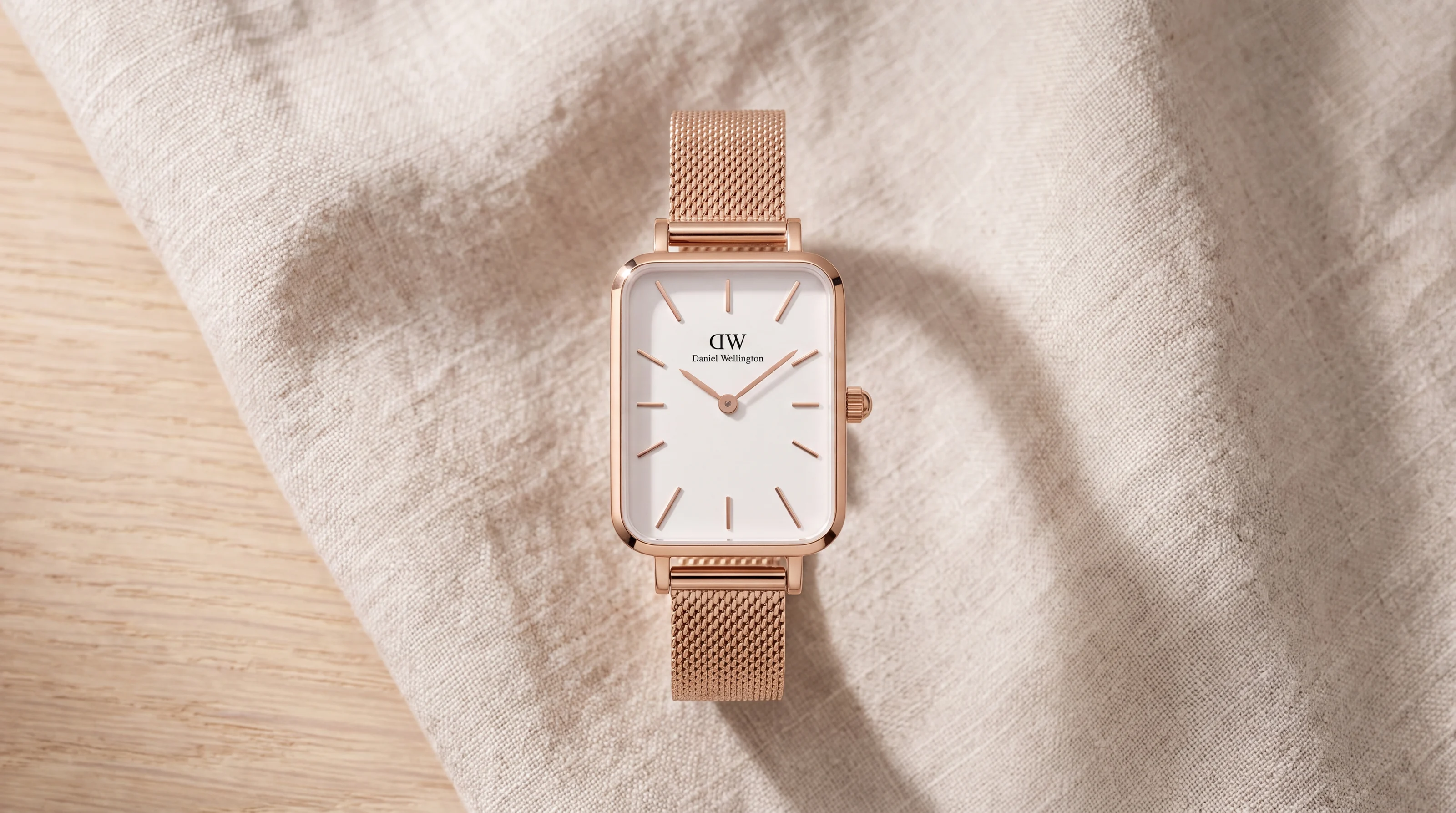 Daniel Wellington Quadro rose gold watch with a white dial resting on linen and light wood