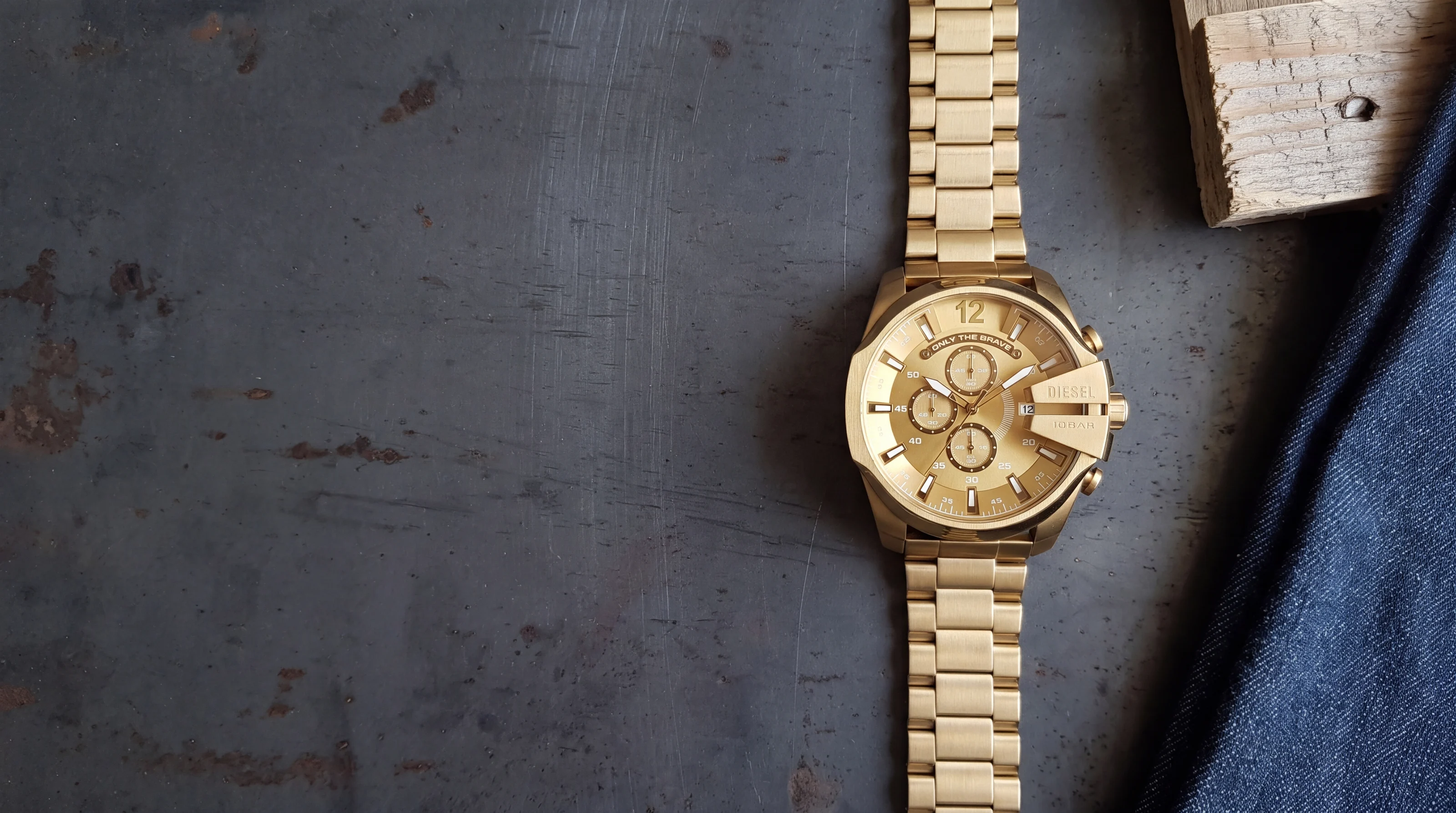 Diesel Mega Chief DZ4360 gold-tone 51 mm chronograph on a patinated steel plate beside raw denim