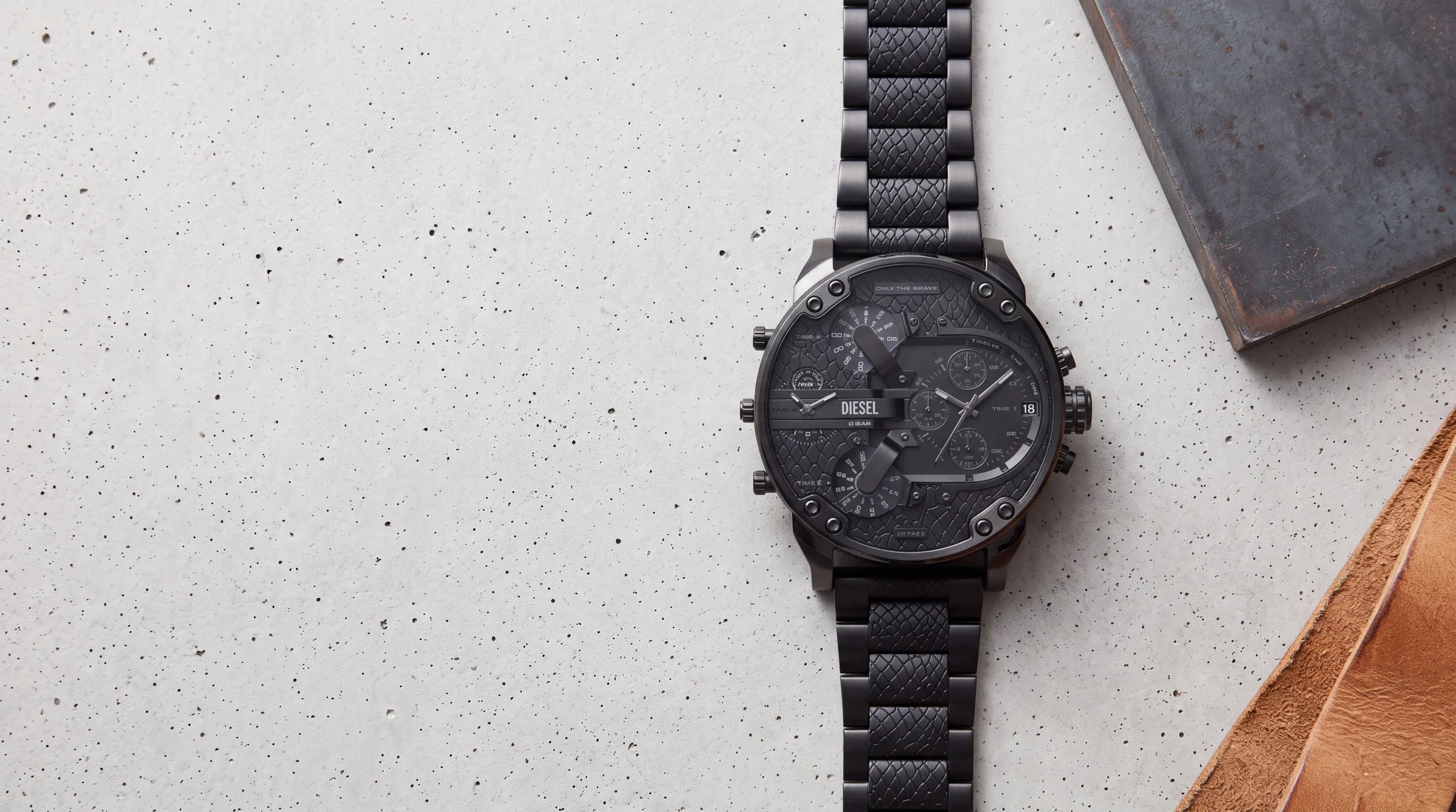 Diesel Mr Daddy 2.0 DZ7468 all-black men's watch with snake-scale dial and links on pale raw concrete