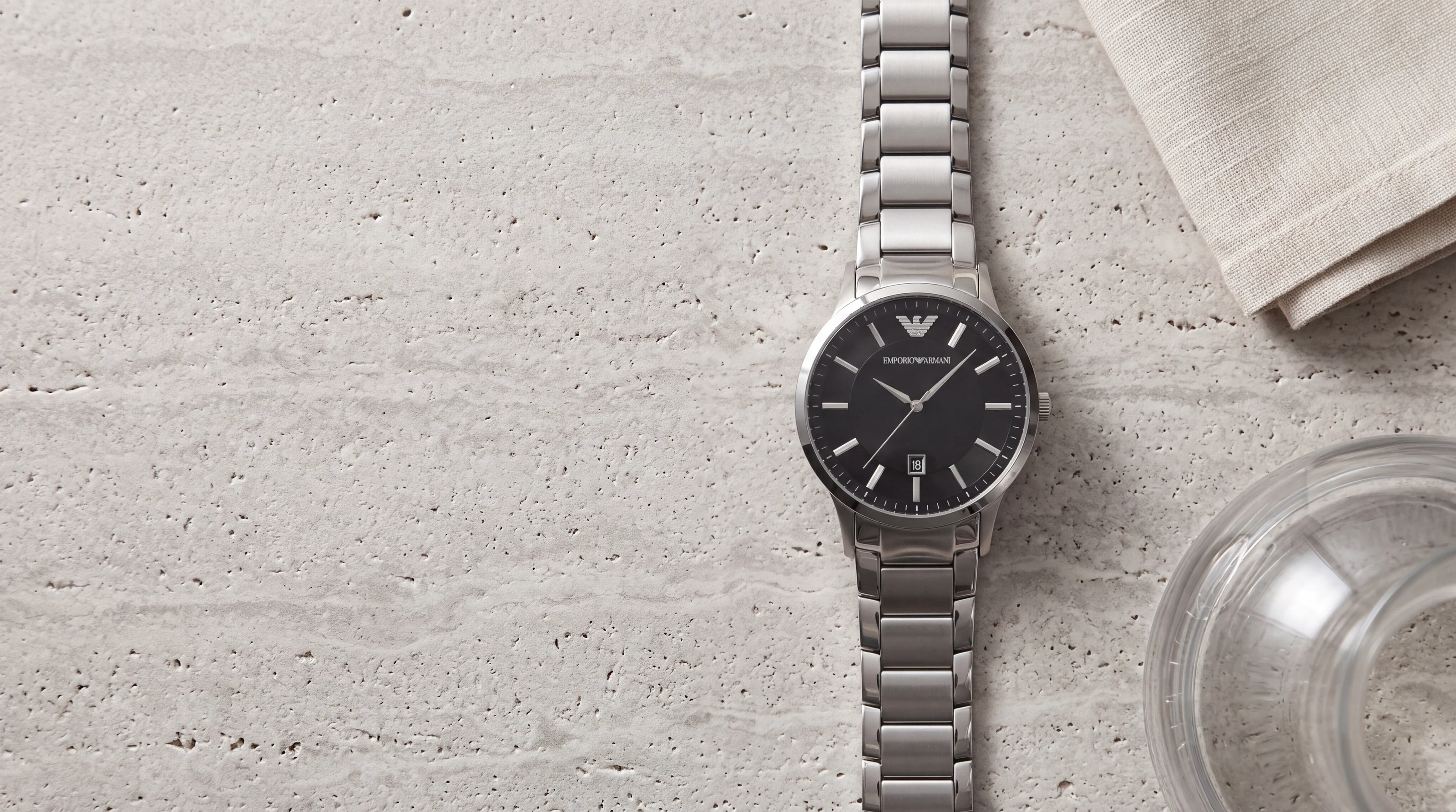 Montre homme Emporio Armani AR2457 en acier, cadran noir et bracelet acier, posée sur du travertin clair