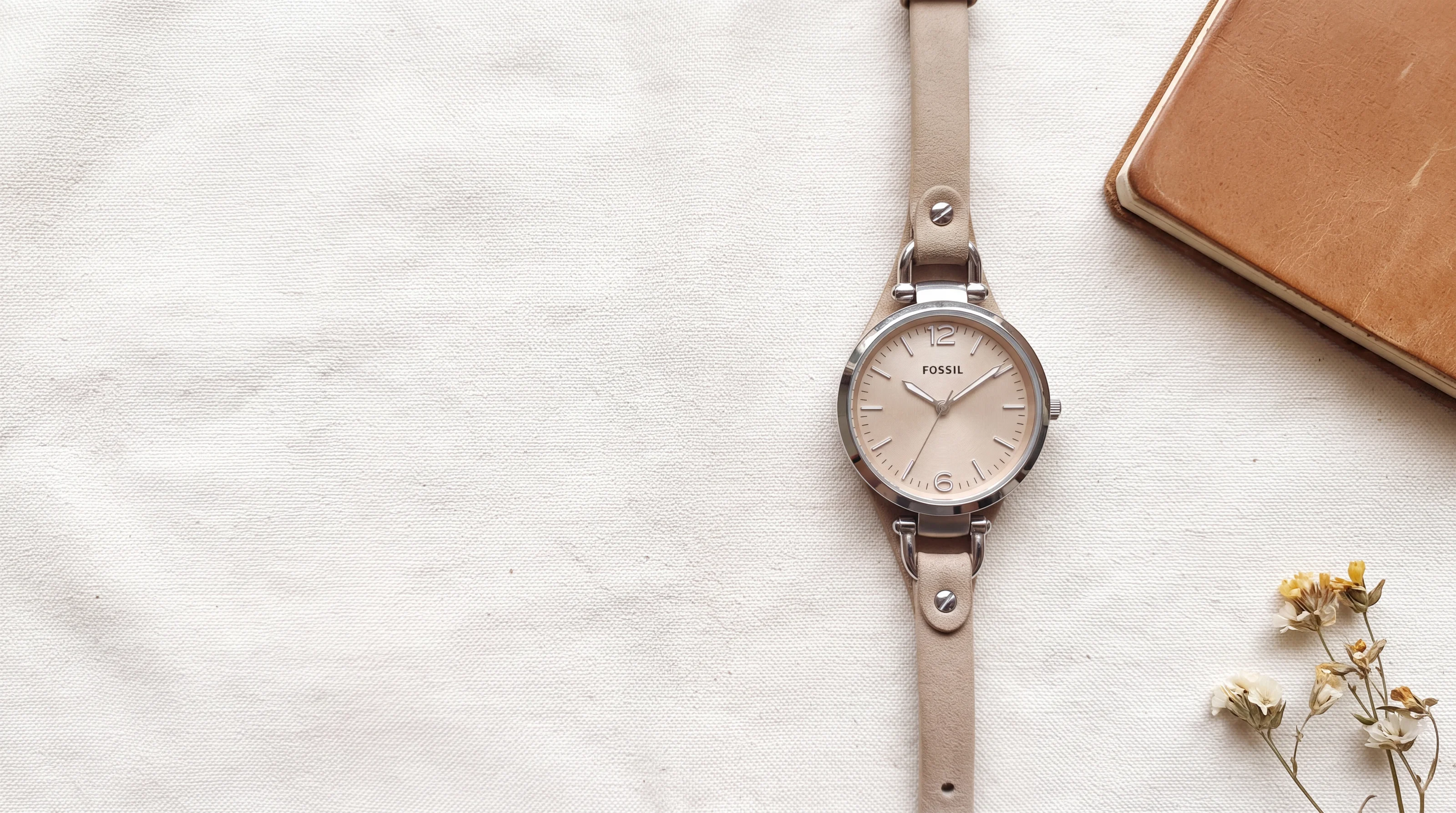 Montre femme Fossil Georgia ES2830 en acier, cadran beige et cuir sable, posée sur toile écrue près de fleurs séchées