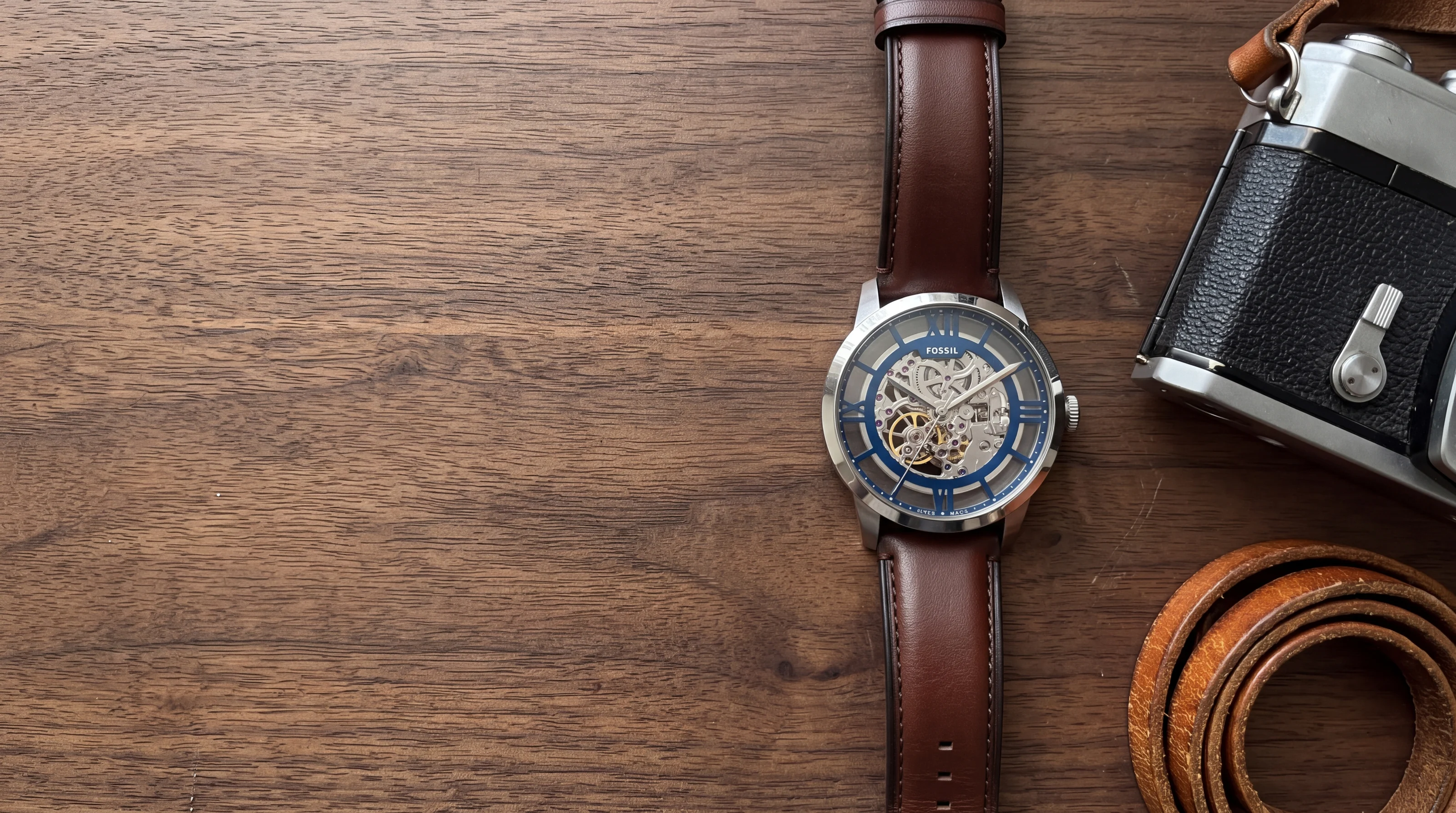 Montre homme Fossil Townsman automatique ME3267 en acier, cadran squelette bleu, sur noyer près d'un appareil argentique
