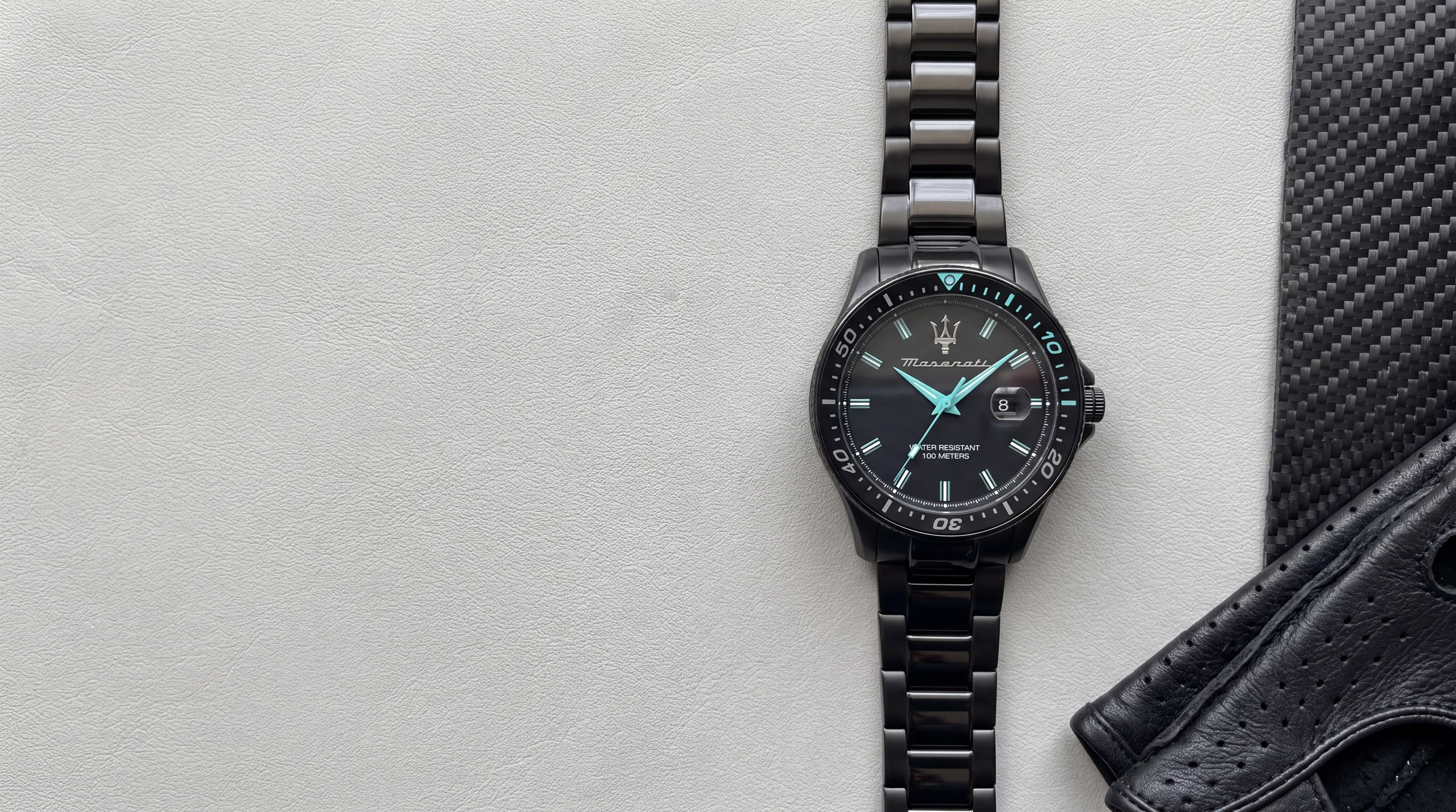 Montre homme MASERATI Sfida Aqua Edition R8853144001 noire à aiguilles turquoise, posée sur cuir gris clair