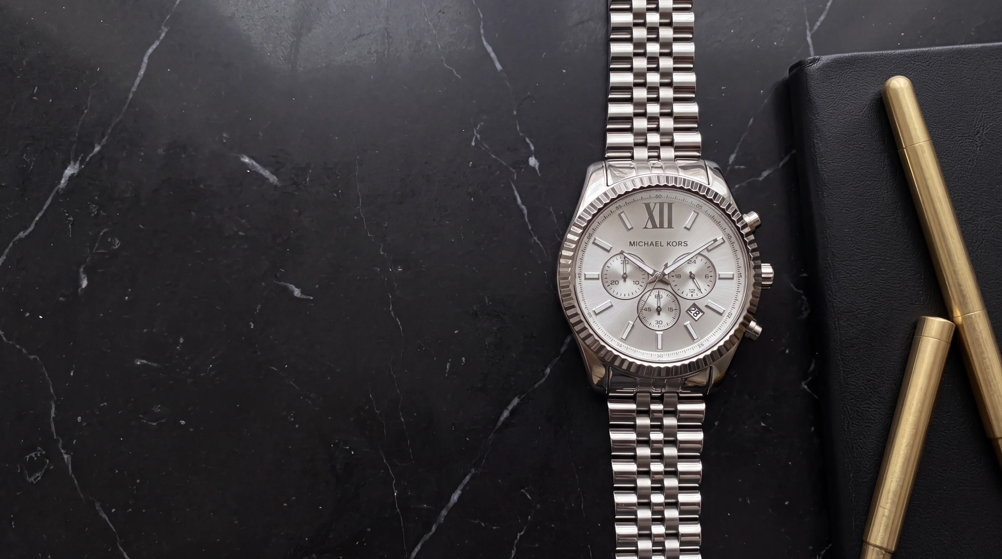 Montre homme Michael Kors Lexington MK8405 en acier, chronographe posé sur marbre noir près d'un carnet en cuir