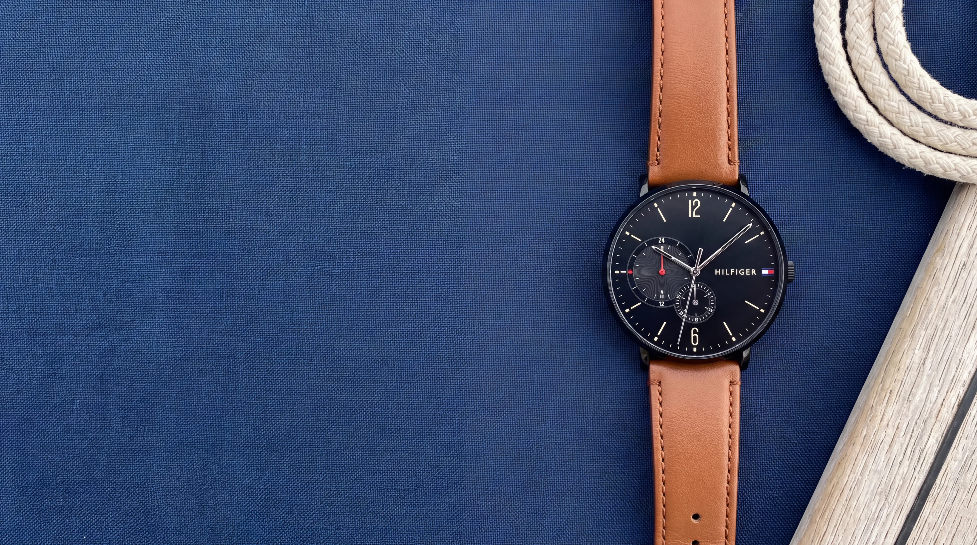 Montre homme Tommy Hilfiger Brooklyn 1791510 noire, bracelet cuir cognac, posée sur du lin bleu marine